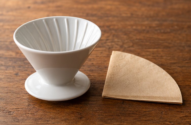 Leerer Handfilter aus weißem Porzellan, daneben ein gefalteter Papierfilter