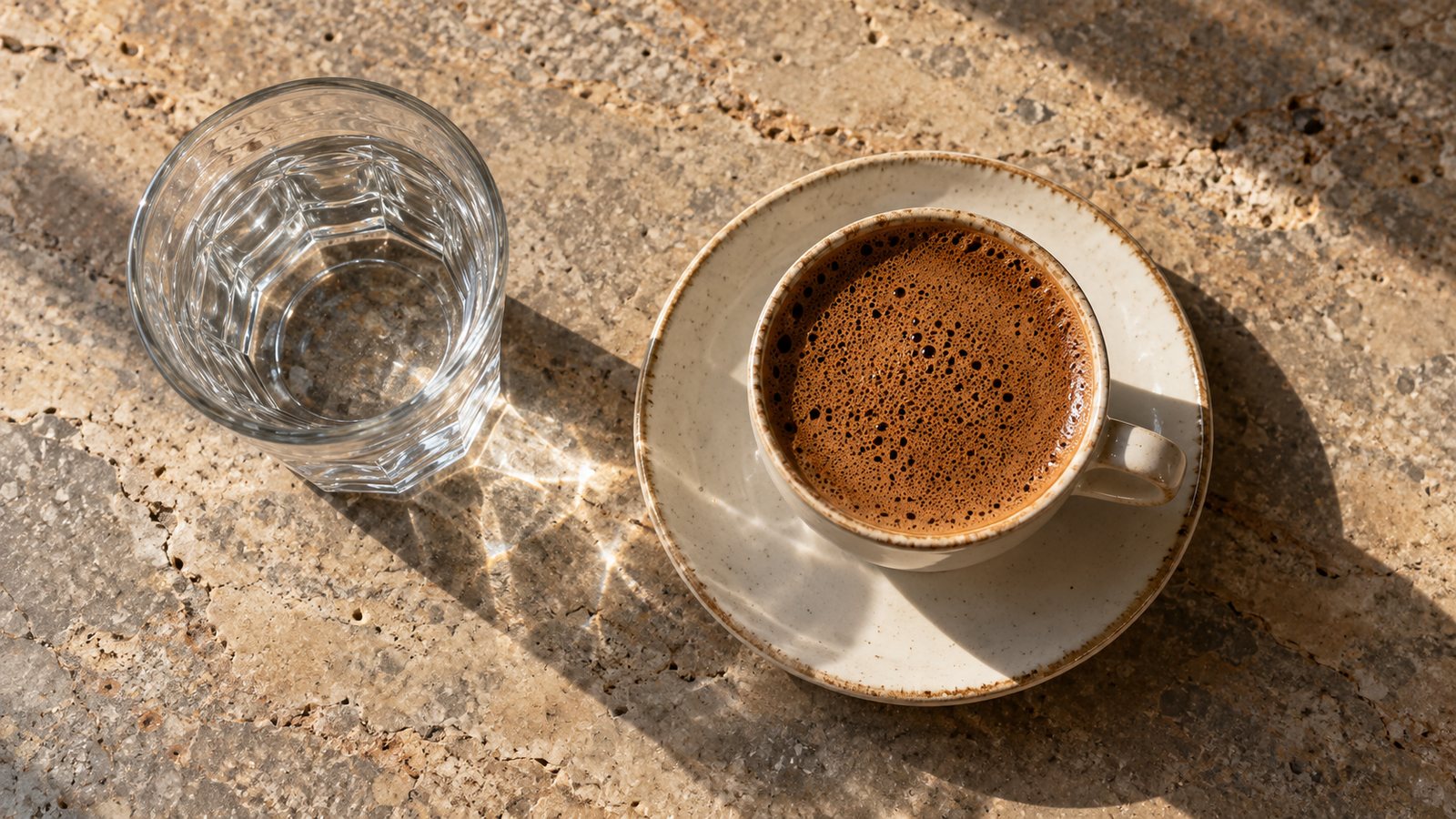 Wie bereitest du türkischen Kaffee zu? Türkischer Mokka mit dichtem Schaum in einer kleinen Porzellantasse, daneben ein Glas Wasser