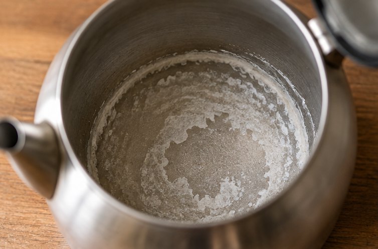Weiße Kalkschicht am Boden eines Wasserkessels aus Metall